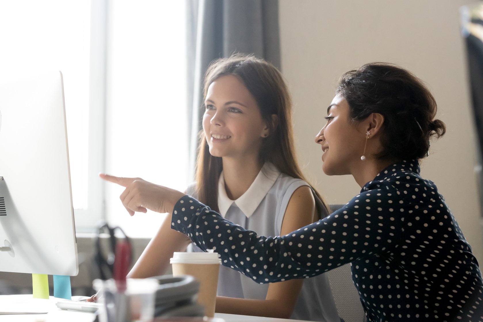 Happy caucasian intern listening to indian mentor explaining computer task